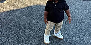Kasizia joined the competition — help win amazing prizes! toddler, child, standing, asphalt, parking_lot, car, black_shirt, beige_pants, white_shoes, curly_hair, urban, outdoor, daylight, shadow, fence, vehicle, side_view, casual_clothing, person, young_child