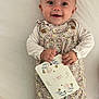 baby, infant, smiling, floral_romper, card, hand, face, blue_eyes, lying_down, white_background, cute, child, person, happy, clothing, button, skin, head, portrait, baby_girl