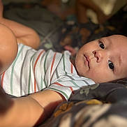 Stylles is registered to the contest to win money with this photo: baby, infant, child, face, eyes, striped_shirt, blanket, bed, reaching, skin, cute, portrait, closeup, lying_down, indoor, soft_light, young, person, focus, cozy