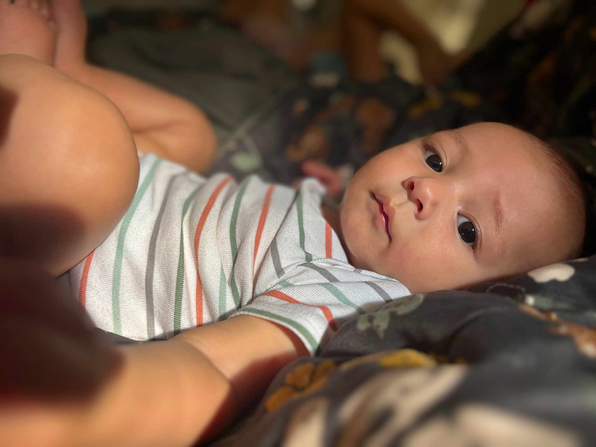 Stylles is registered to the contest to win money with this photo: baby, infant, child, face, eyes, striped_shirt, blanket, bed, reaching, skin, cute, portrait, closeup, lying_down, indoor, soft_light, young, person, focus, cozy