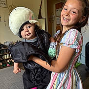 Stylles is registered to the contest to win money with this photo: child, baby, girl, smile, indoor, plush_hat, jacket, dress, happy, person, home, shoes, furniture, toy, living_room, cute, holding, playful, family, portrait