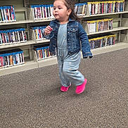 Ruby is registered to the contest to win money with this photo: toddler, child, running, denim_jacket, blue_jumpsuit, pink_shoes, carpet, bookshelf, library, indoor, person, young_child, hair, clothing, shelf, floor, motion, aisle, casual, cute