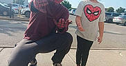 Raelynn is registered to the contest to win money with this photo: cars, child, clouds, costume, crouching, mask, outdoor, parking_lot, playful, portrait, sidewalk, sky, smiling, sneakers, spiderman, standing, sunny, superhero, thumbs_up, tshirt