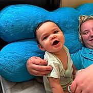 Toebias is registered to the contest to win money with this photo: baby, child, infant, smiling, sitting, portrait, face, person, adult, parent, blue_pillow, bed, bedroom, indoor, clothing, short_sleeves, family, happy, caregiving, photography