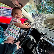 Toebias is registered to the contest to win money with this photo: adult, air_freshener, automotive_interior, baby, car, child, dashboard, daylight, driver_seat, family, hand, happy, infant, outdoor, portrait, red_car, smiling, steering_wheel, striped_clothing, vehicle