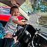 baby, child, infant, smiling, happy, car, vehicle, steering_wheel, dashboard, driver_seat, adult, hand, outdoor, daylight, red_car, striped_clothing, air_freshener, automotive_interior, portrait, family