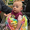 Rosaleigh joined the competition — help win amazing prizes! baby, shopping_cart, blanket, colorful, child, person, indoor, retail, store, shelf, clothing, hand, face, expression, curious, sitting, toy, safe, adult_arm, rainbow