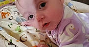 Rosaleigh is registered to the contest to win money with this photo: baby, child, infant, pajamas, purple_clothing, blanket, alphabet, face, indoor, furniture, couch, curious, lying_down, young_child, soft_toys, head, hand, cozy, portrait, closeup