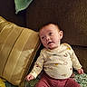 baby, child, infant, couch, pillow, blanket, clothing, patterned, onesie, pink_pants, face, expression, indoor, cozy, seated, looking_up, curious, home, soft_lighting, relaxed