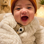 Elias is registered to the contest to win money with this photo: baby, child, smiling, beanie, teddy_bear, plush, warm_clothing, indoor, cute, happy, cozy, soft_lighting, portrait, infant, face, apparel, toy, cute_expression, fuzzy_texture, nursery