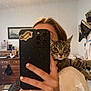 Franklin is registered to the contest to win money with this photo: cat, tabby_cat, person, selfie, mirror, phone, hand, fingernails, sticker, hot_dog_sticker, bedroom, dresser, clothing, furniture, indoor, curious_cat, reflection, white_shirt, animal, pet
