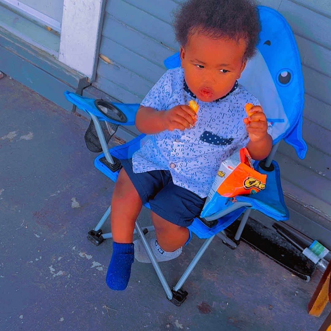 Jakyree joined the competition — help win amazing prizes! blue_chair, blue_socks, chair, child, clothing, concrete_floor, curious_expression, door, food, heart_emoji, outdoor, porch, shark_design, shirt, shorts, sitting, snack, toddler, wall, wooden_table