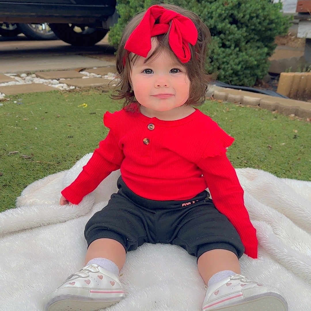 Sarah Bejarano is registered to the contest to win money with this photo: toddler, child, red_clothing, headband, bow, sneakers, white_blanket, outdoor, grass, greenery, bush, vehicle, black_car, shorts, cute, sitting, portrait, baby, happy, fashion