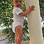 baby, toddler, child, standing, white_onesie, barefoot, pillar, stone_surface, outdoor, greenery, leaves, smiling, happy, person, nature, daylight, cute, curious, holding, balance
