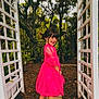 Lilly is registered to the contest to win money with this photo: child, girl, pink_dress, smiling, outdoor, garden, pathway, trees, plants, trellis, nature, happy, posing, footwear, casual, young, playful, daylight, greenery, portrait