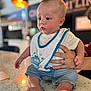 baby, bib, blurred_background, casual_clothing, child, countertop, cute, feet, focus, hand, indoor, infant, jeans, person, portrait, ring, sitting, speckled_surface, support, young