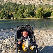 Cameron a rejoint le concours — aidez-le/la à gagner de superbes lots ! baby, blue_sky, child, clothing, cozy, daytime, forest, happy, mountain, nature, outdoor, person, riverbank, sand, scenic, smiling, stroller, sunlight, toy, trees