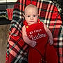 Greyson joined the competition — help win amazing prizes! baby, infant, red_clothing, knitwear, plaid_blanket, christmas, holiday, child, indoors, furniture, bookshelf, flooring, face, person, festive, cute, portrait, sitting, cozy, warm_colors