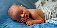 Greyson is registered to the contest to win money with this photo: baby, newborn, sleeping, infant, blue_blanket, striped_cloth, peaceful, face, hand, skin, closeup, soft_texture, lying_down, resting, cute, portrait, child, toddler, indoors, comfort