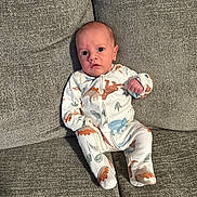 Greyson joined the competition — help win amazing prizes! baby, infant, child, pajamas, dinosaur_print, sitting, couch, sofa, gray, fabric, indoor, cute, expression, face, small, cozy, clothing, person, newborn, home