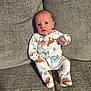 baby, infant, child, pajamas, dinosaur_print, sitting, couch, sofa, gray, fabric, indoor, cute, expression, face, small, cozy, clothing, person, newborn, home