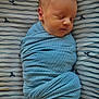 newborn, baby, sleeping, swaddled, blue_blanket, striped_sheet, whale_pattern, infant, peaceful, soft_texture, wrapped, portrait, closeup, face, head, resting, cute, child, indoors, cozy