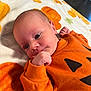 baby, blanket, child, cozy, curious, cute, face, fall_theme, fist, indoor, infant, lying_down, newborn, orange_clothing, portrait, pumpkin, sleepwear, small_hands, soft_texture, toddler