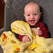 Greyson is registered to the contest to win money with this photo: baby, blanket, smiling, child, infant, red_clothing, yellow, duck_pattern, cozy, indoor, cushion, happy, face, cute, young_child, seated, cheerful, portrait, hands, head