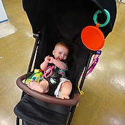 Sylvia joined the competition — help win amazing prizes! baby, baby_toy, black, child, clothing, colorful, cute, floor, foot, happy, indoor, infant, person, play, seat, shopping, smile, store, stroller, toy