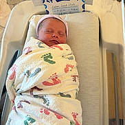 Caden is registered to the contest to win money with this photo: newborn, baby, swaddled, blanket, hospital, bassinet, sleeping, infant, footprints, card, announcement, boy, hat, peaceful, indoors, portrait, child, bed, comfort, resting