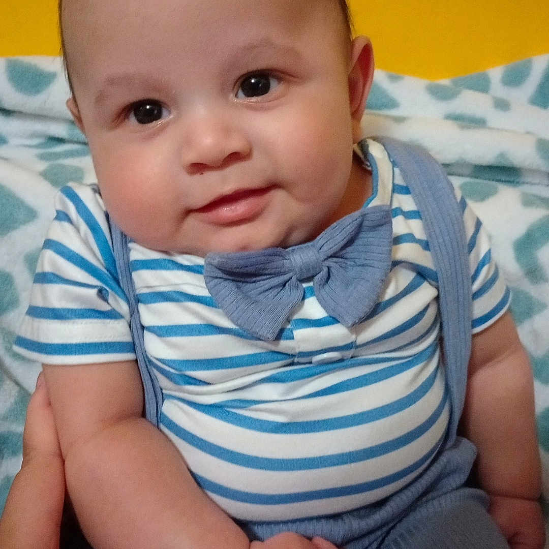 Makiah joined the competition — help win amazing prizes! baby, blanket, blue_pants, bow_tie, cheeks, child, clothing, cute, face, hand, holding, indoors, infant, person, portrait, sitting, smile, striped_shirt, yellow_wall, young
