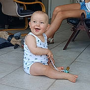 Maé participe au concours pour gagner de l'argent avec cette photo : baby, child, indoor, floor, tile, pacifier, chain, dog, pet, chair, legs, person, white_clothing, smiling, happy, casual, home, relaxed, cute, infant