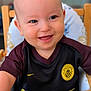 baby, child, smiling, high_chair, clothing, jersey, manchester_city, happy, face, infant, person, table, wood, seat, cute, portrait, indoor, sportswear, small_child, cheerful