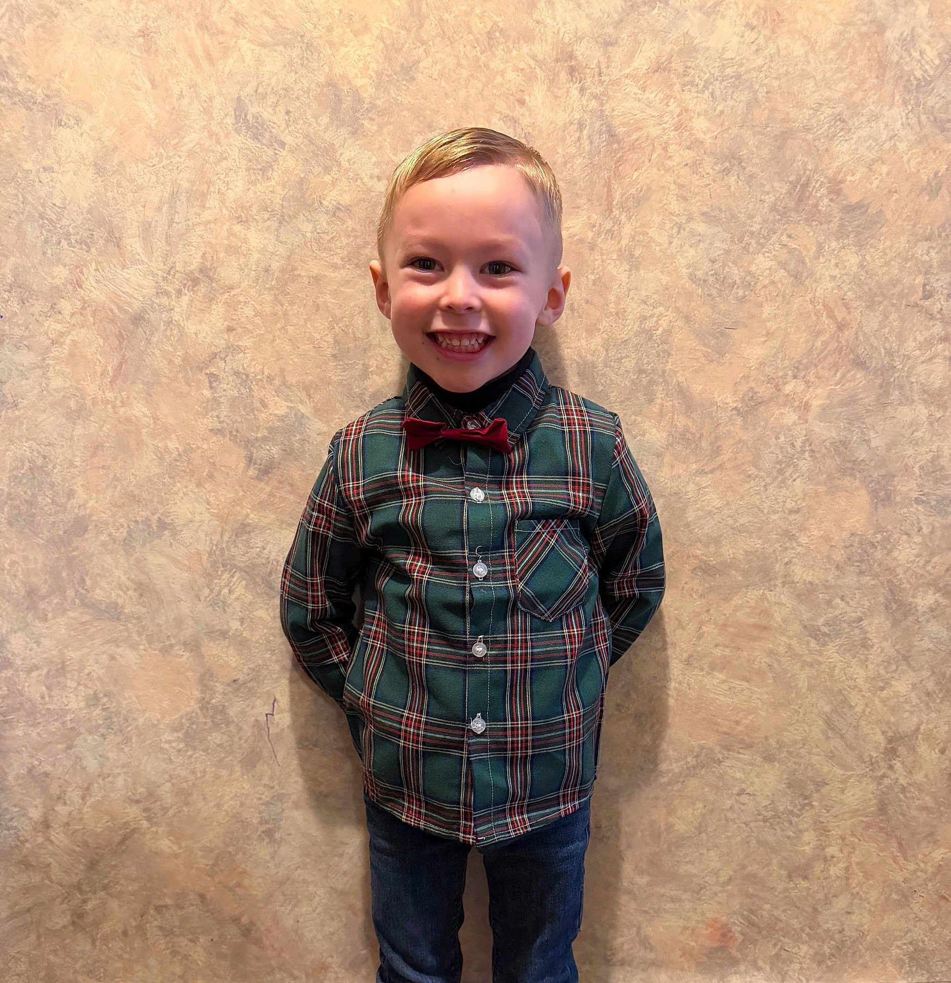 Adriano a rejoint le concours — aidez-le/la à gagner de superbes lots ! child, boy, smiling, plaid_shirt, bow_tie, jeans, standing, indoor, wall, beige_background, happy, portrait, fashion, casual, cute, hands_behind_back, short_hair, young, person, face