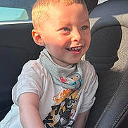 Adriano participe au concours pour gagner de l'argent avec cette photo : child, boy, smile, happy, car_seat, tshirt, blonde_hair, blue_eyes, sunlight, indoors, seat, clothing, face, person, portrait, casual, cute, baby_bib, vehicle, window