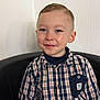 armchair, boy, button_down, casual_clothing, cheek, child, collar, ear, eyes, groomed_hair, happy, indoor, plaid_shirt, pocket, portrait, seated, short_hair, smile, textured_wall, toddler
