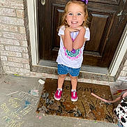 Brixlyn is registered to the contest to win money with this photo: child, girl, purple_bow, white_tshirt, denim_shorts, pink_shoes, welcome_mat, chalk_drawings, concrete_floor, wooden_door, brick_wall, smiling, posing, outdoor, front_porch, happy, casual_clothing, young_child, daylight, playful