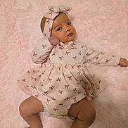 River is registered to the contest to win money with this photo: arms, baby, blanket, bow, child, cozy, cute, dress, foot, hand, headband, indoors, infant, laying, legs, patterned_clothing, pink, portrait, skin, soft_texture