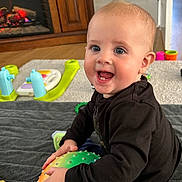 Bailey is registered to the contest to win money with this photo: baby, child, indoors, toys, ball, colorful, happy, smiling, blanket, fireplace, floor, wood, clothing, person, play, hand, face, blue_eyes, sitting, mohawk