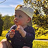 baby, casual_clothing, child, cute, daylight, face, flower, grass, greenery, hat, nature, outdoor, person, playing, sitting, summer, sunlight, tree, yellow_cap, young_child
