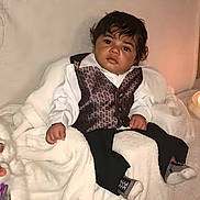 Aaron is registered to the contest to win money with this photo: baby, child, portrait, sitting, indoors, formal_clothing, white_shirt, vest, black_pants, chair, snowman, plush_toy, candles, warm_lighting, holiday, cozy, face, dark_hair, serious_expression, photography