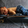 baby, newborn, sleeping, skateboard, jeans, clothing, soft_pillow, gray_background, infant, peaceful, portrait, cute, child, resting, floor, studio, casual, small, horizontal, toddler