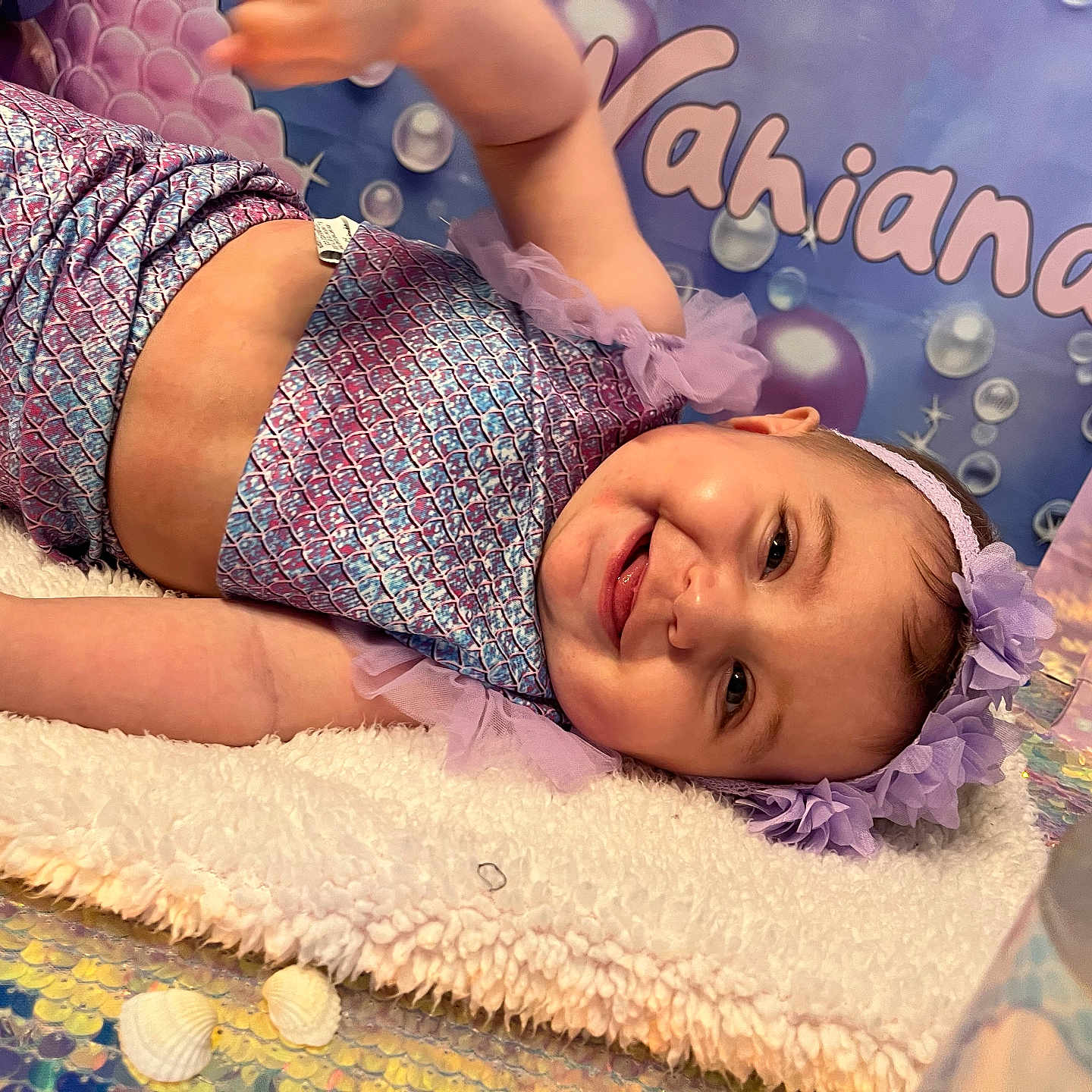 Khaïna a rejoint le concours — aidez-le/la à gagner de superbes lots ! baby, balloons, blanket, celebration, child, cute, decorations, face, hand, happy, headband, indoors, mermaid_outfit, name, party, portrait, purple, shells, smiling, table
