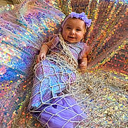 Khaïna participe au concours pour gagner de l'argent avec cette photo : baby, child, smile, face, mermaid_costume, purple, headband, sequin_blanket, net, pillow, indoor, tulle, fabric, cute, lying_down, playful, costume, portrait, colorful, happy