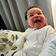 Alora joined the competition — help win amazing prizes! baby, infant, smile, joy, onesie, white_clothing, colorful_stars, curtains, blanket, leaf_pattern, hand, indoor, happy, face, cute, child, young, person, cozy, fun