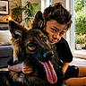 animal, boy, carpet, child, couch, dog, family, german_shepherd, happy, houseplant, hugging, indoor, living_room, pet, portrait, smiling, sunlight, tongue, window, wooden_interior
