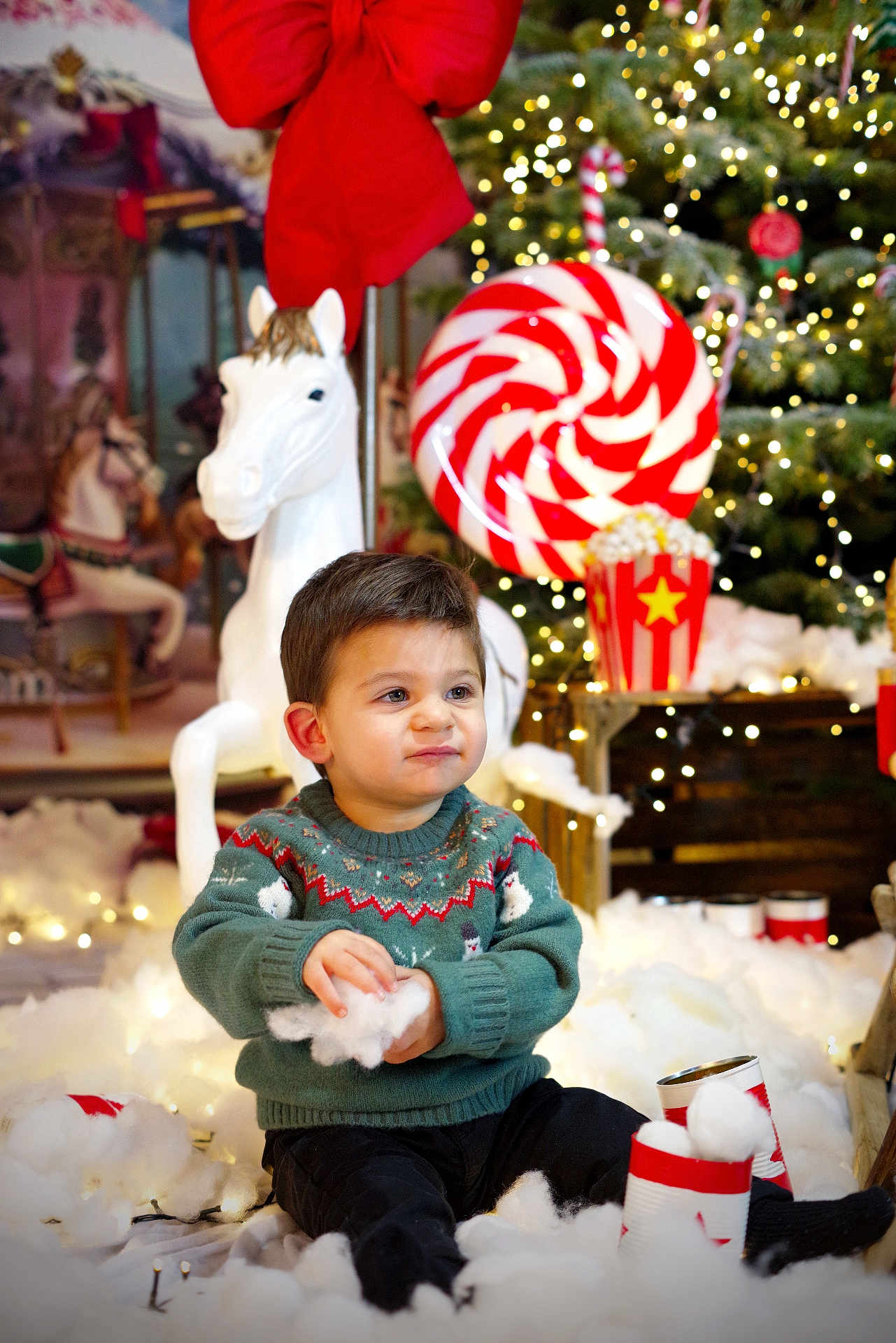 Ilyas a rejoint le concours — aidez-le/la à gagner de superbes lots ! toddler, child, sweater, holiday, christmas, decorations, cotton, fake_snow, toy_horse, candy, lights, festive, smiling, indoor, seasonal, cute, red, green, playful, winter