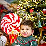 child, toddler, smile, sweater, holiday, christmas_tree, lights, decorations, candy, popcorn, chair, indoors, festive, happy, winter, face, person, toy, background, celebration