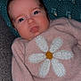baby, infant, sweater, flower, daisy, pink_clothing, blue_eyes, hand, cushion, pattern, texture, indoor, portrait, child, cute, cozy, resting, fabric, knitwear, casual
