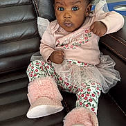 Khalani is registered to the contest to win money with this photo: baby, child, infant, pink_clothing, floral_pattern, tutu, boots, fur_boots, leather_chair, curly_hair, hair_bow, sitting, portrait, indoor, cute, expression, wide_eyes, fist, young_child, adorable